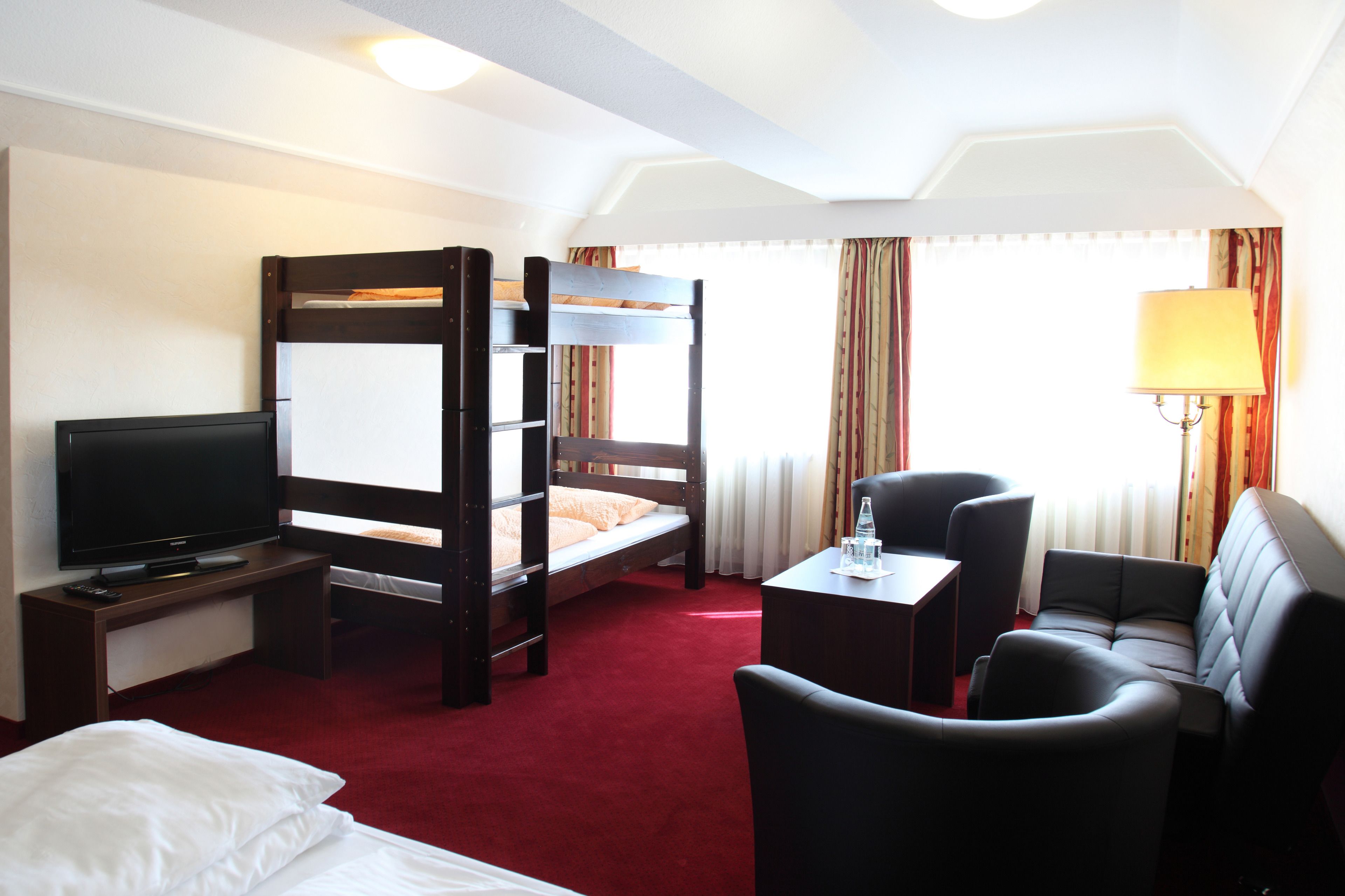 A hotel room with a bunk bed, a TV, a desk with a lamp, and a sofa.