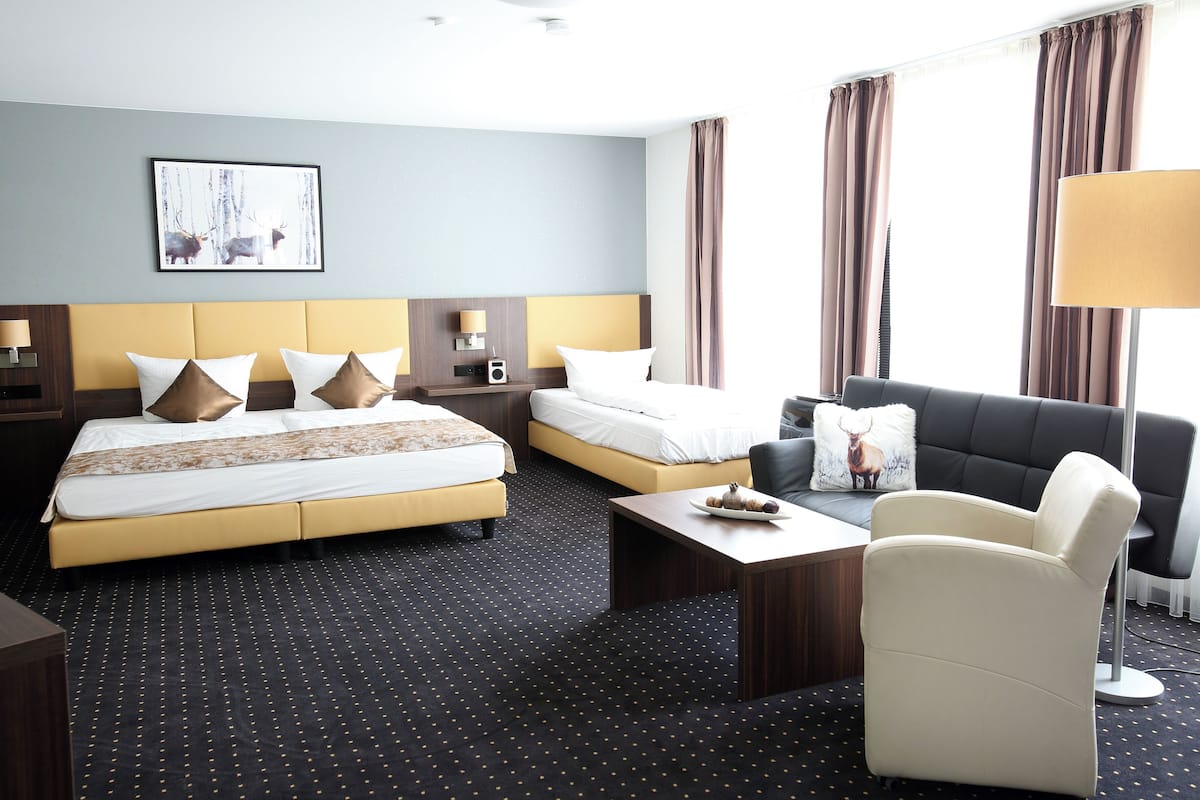 A hotel room with two beds, a sofa, a coffee table, and a lamp.
