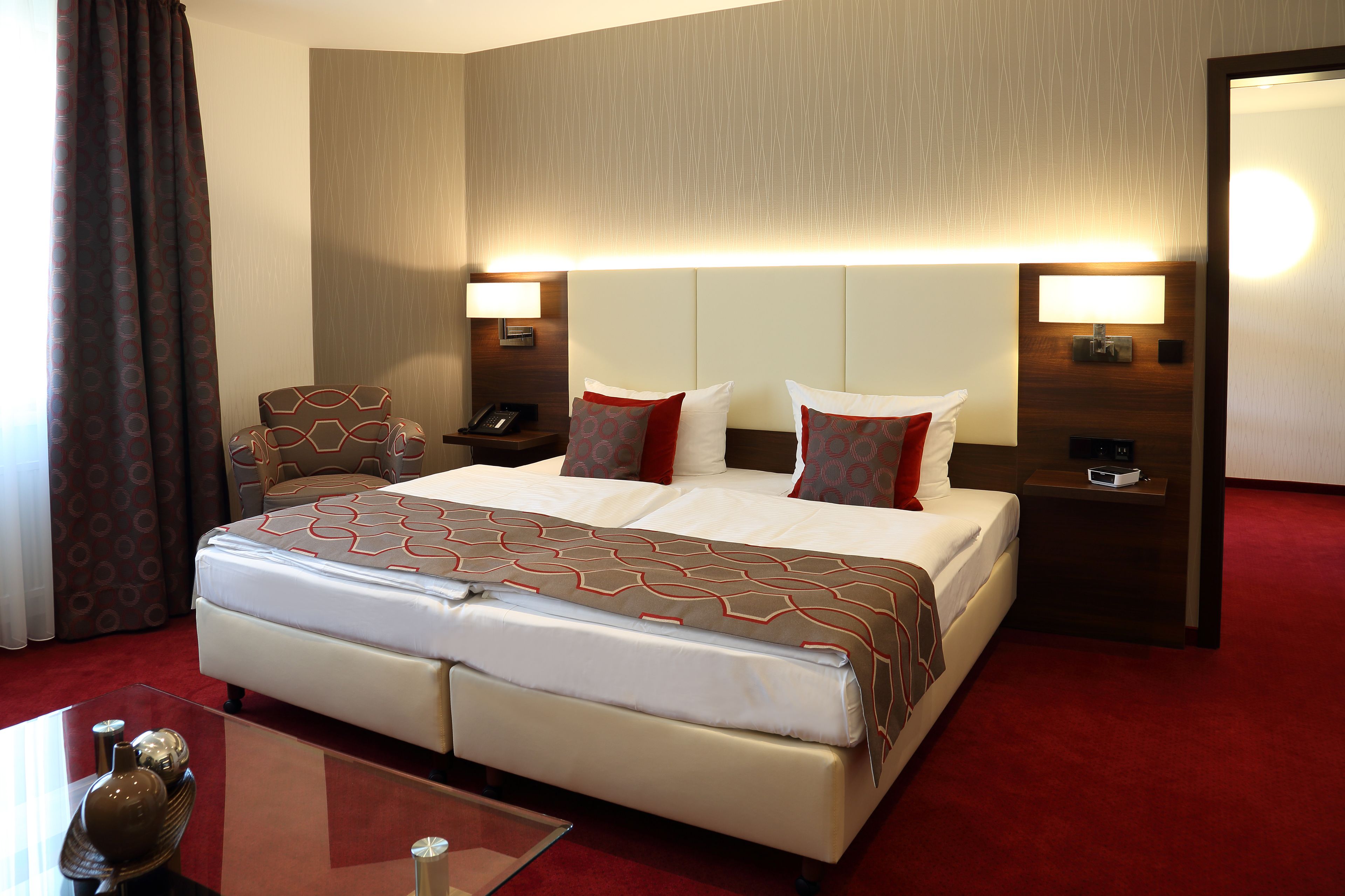 Una habitación de hotel con una cama grande, dos mesitas de noche, una silla, un escritorio y un espejo.
