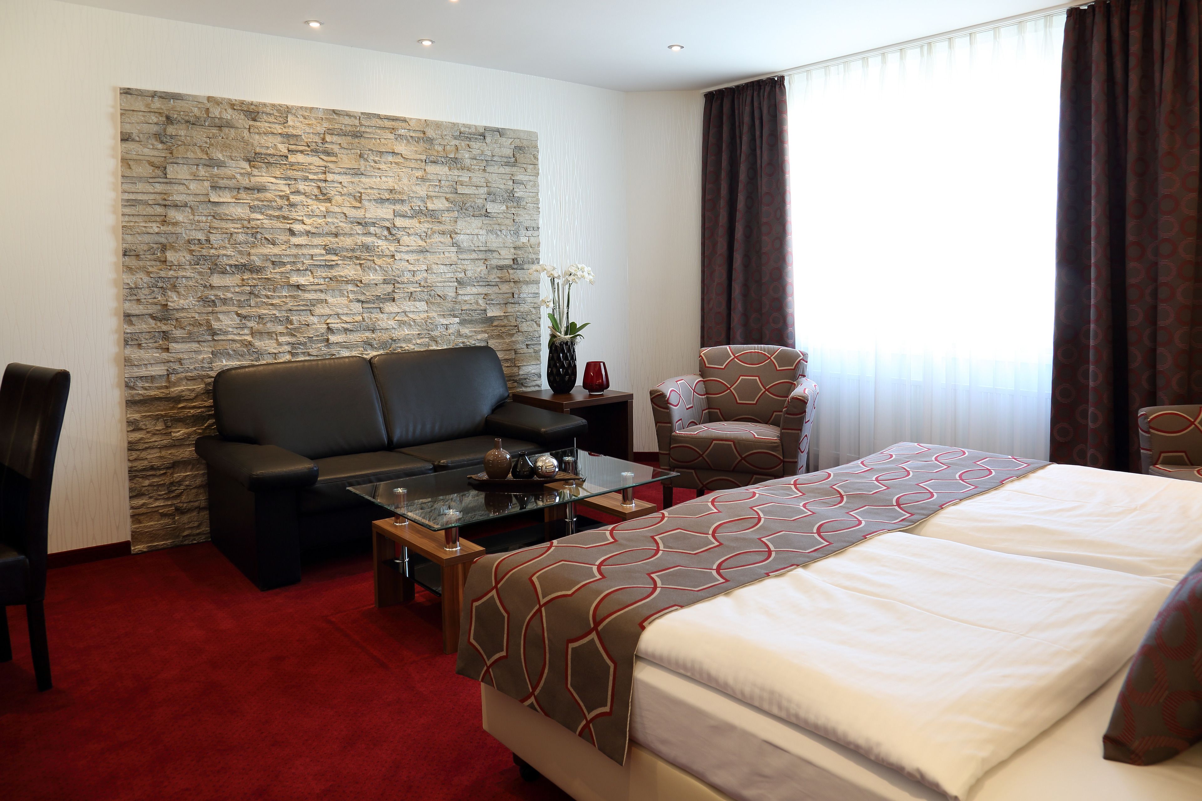 A hotel room with a stone accent wall, a large bed with patterned bedding, a sofa, a coffee table, and a chair.