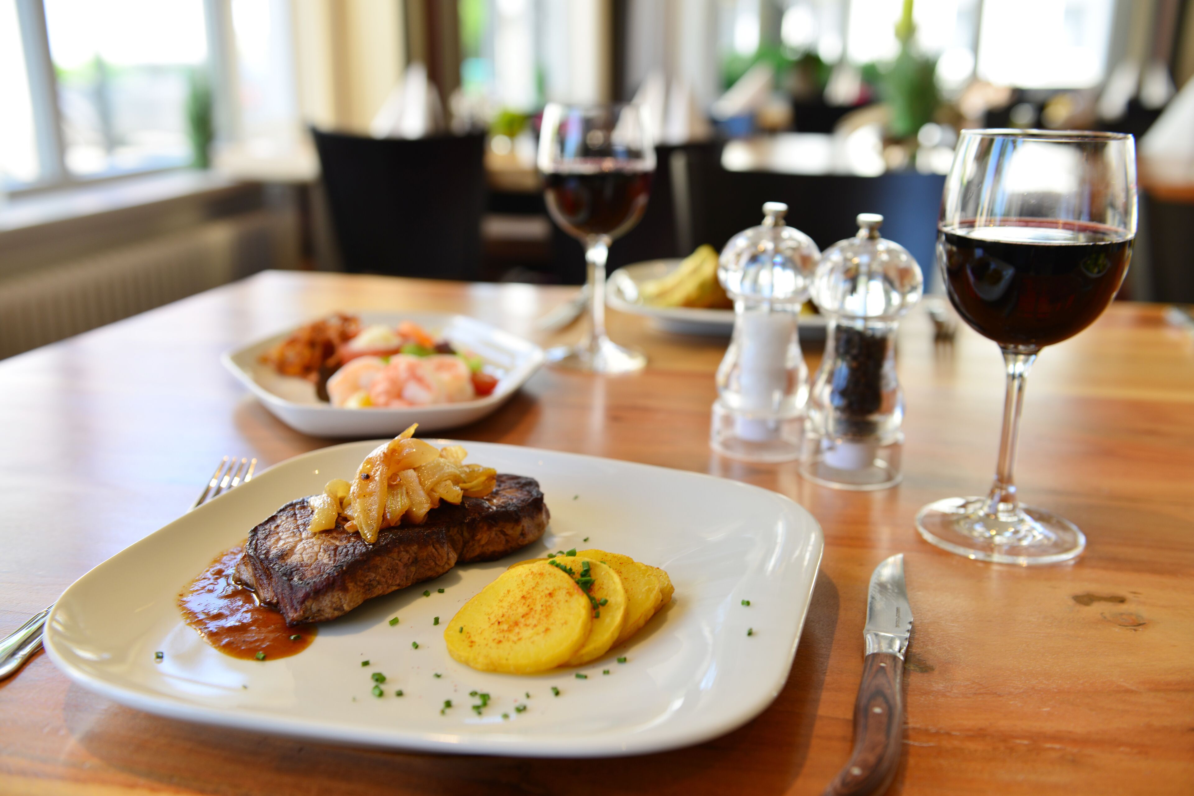 A dining table with a plate of steak, potatoes, and a glass of red wine.