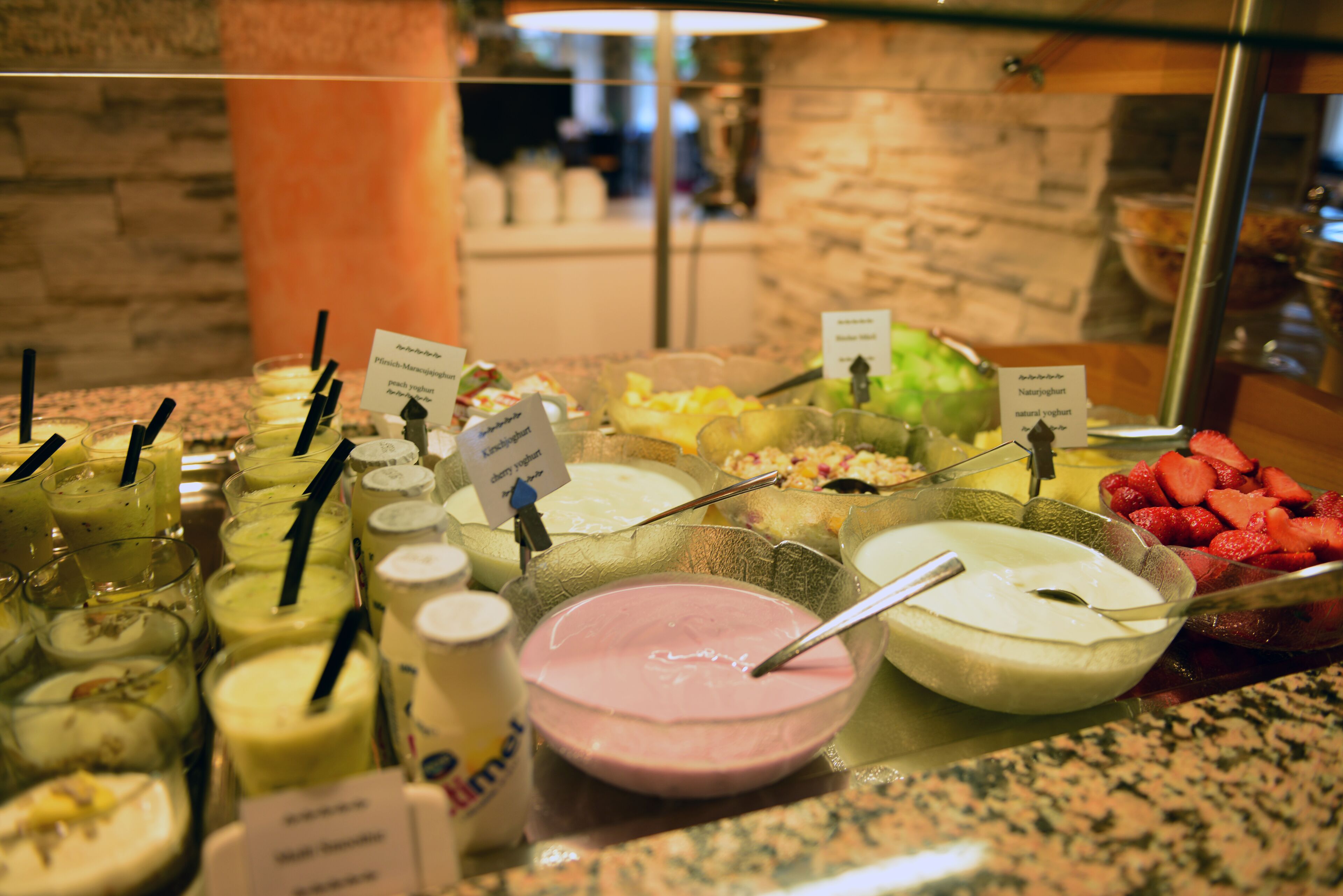 Buffet com diversos alimentos e bebidas, incluindo uma tigela de sobremesa cor-de-rosa e uma tigela de sobremesa branca.