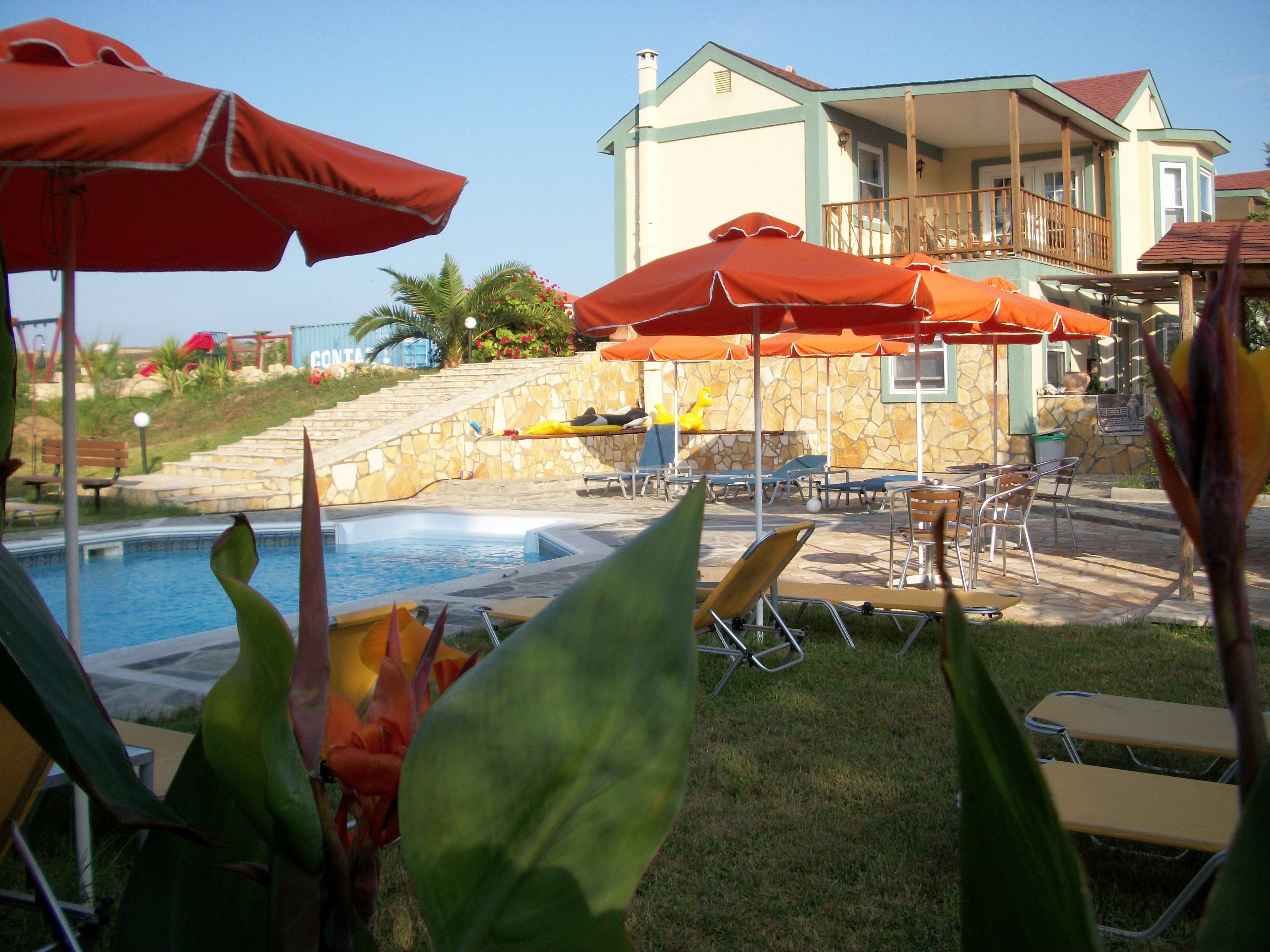 A pool area with lounge chairs and umbrellas, a stone staircase, and a building with a balcony.