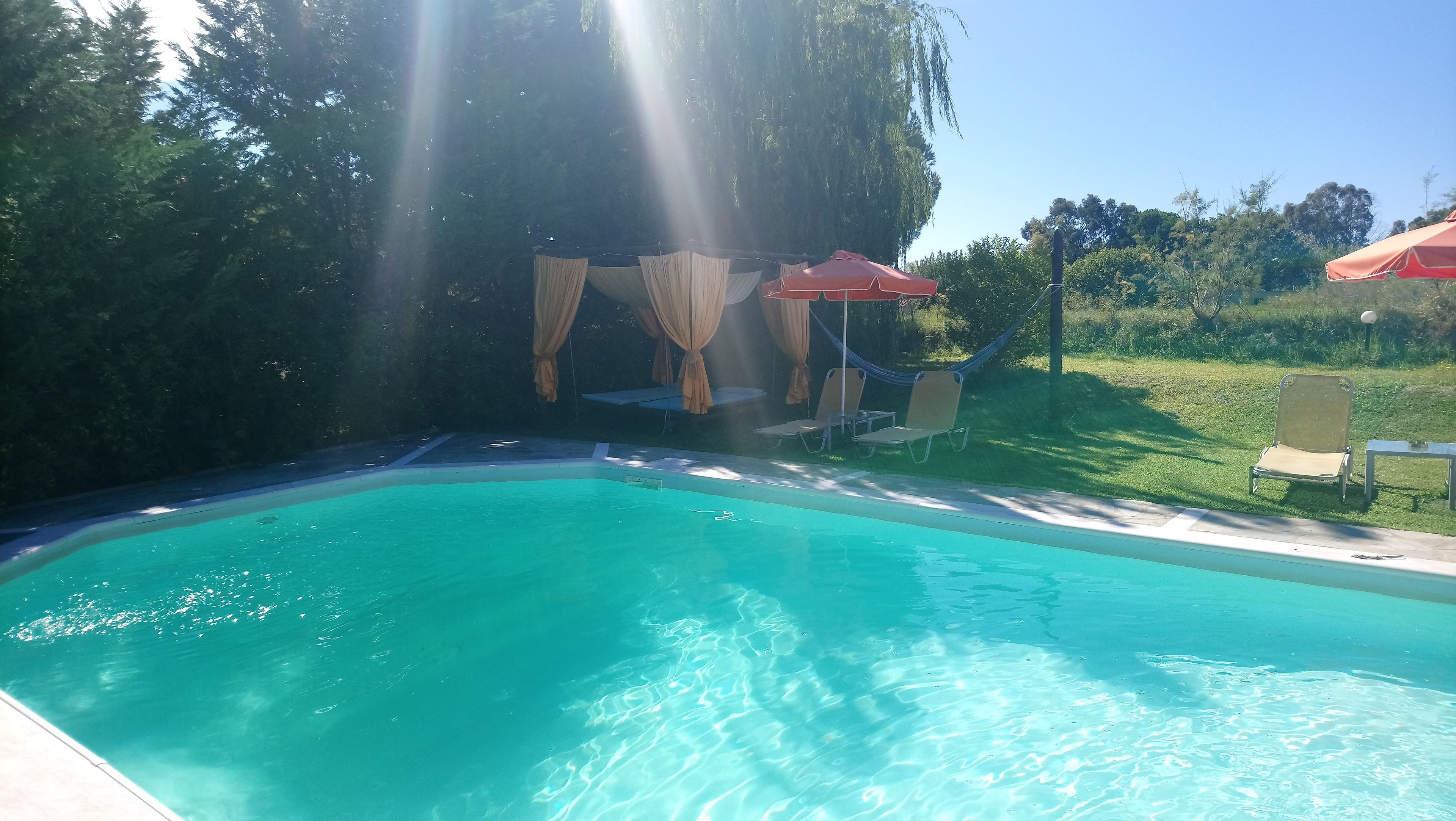 A clear swimming pool with a sunlit area featuring a canopy and chairs.