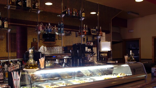 Een bar met een vitrine vol eten, een koffieapparaat en diverse flessen op planken.