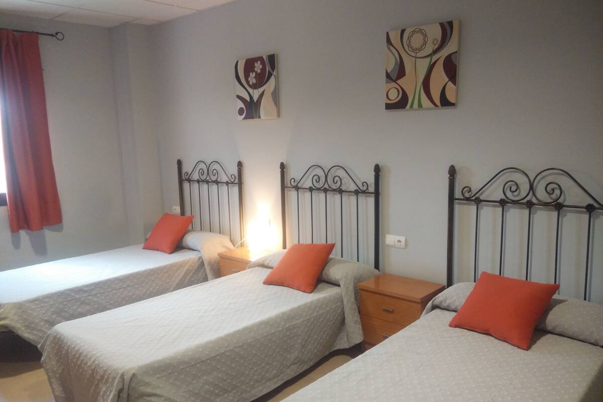 Une chambre avec trois lits simples, chacun étant équipé d’un oreiller et d’une table de chevet.