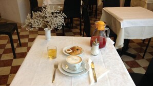 Una mesa de comedor con mantel blanco, una taza de té, un plato con croissants, una taza de café y un azucarero.