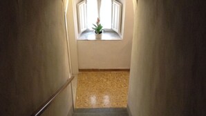 Una escalera estrecha que lleva a un rellano con un ventanal pequeño.