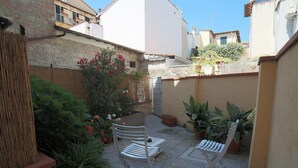 Un pequeño patio al aire libre con dos sillas blancas, plantas en macetas y una valla de bambú.