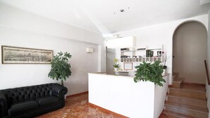 Amplia sala de estar con un sofá de cuero negro, un mostrador de recepción blanco y una escalera que conduce a un piso superior.