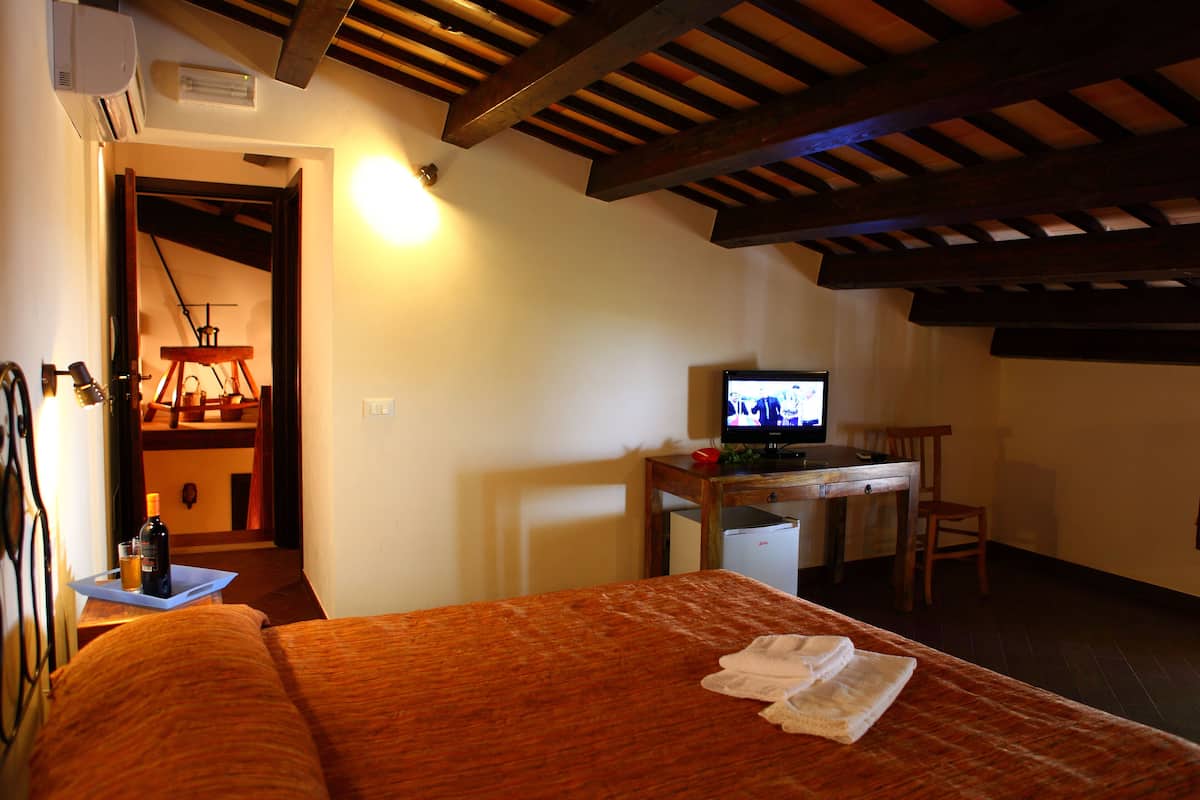 A hotel room with a bed, a desk with a television, a chair, and a small table with a bottle and glass.