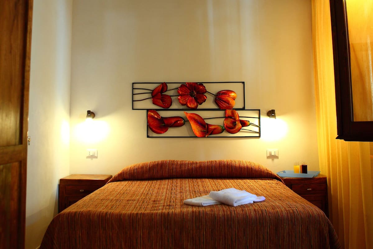 A bedroom with a large bed, wooden headboard, and a wall-mounted artwork.