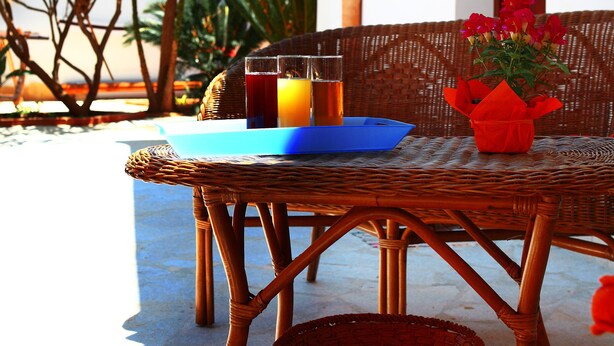 A wicker table with a blue tray, a glass of orange juice, and a red vase with flowers. - Bed & Breakfast Sabir (San Vito Lo Capo)