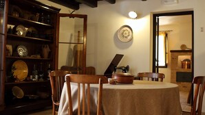 A dining area with a round table covered by a beige tablecloth, surrounded by wooden chairs. A wooden cabinet with dishes is to the left. - Bed & Breakfast Sabir (San Vito Lo Capo)