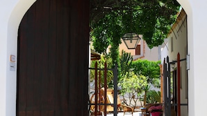 An arched entrance with a dark wooden door, a stone-paved pathway, and a view of a courtyard with furniture and plants. - Bed & Breakfast Sabir (San Vito Lo Capo)
