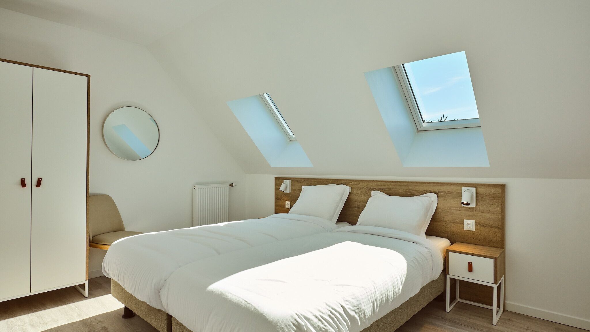 A bedroom with a large bed, a wardrobe, a round mirror, and skylights.