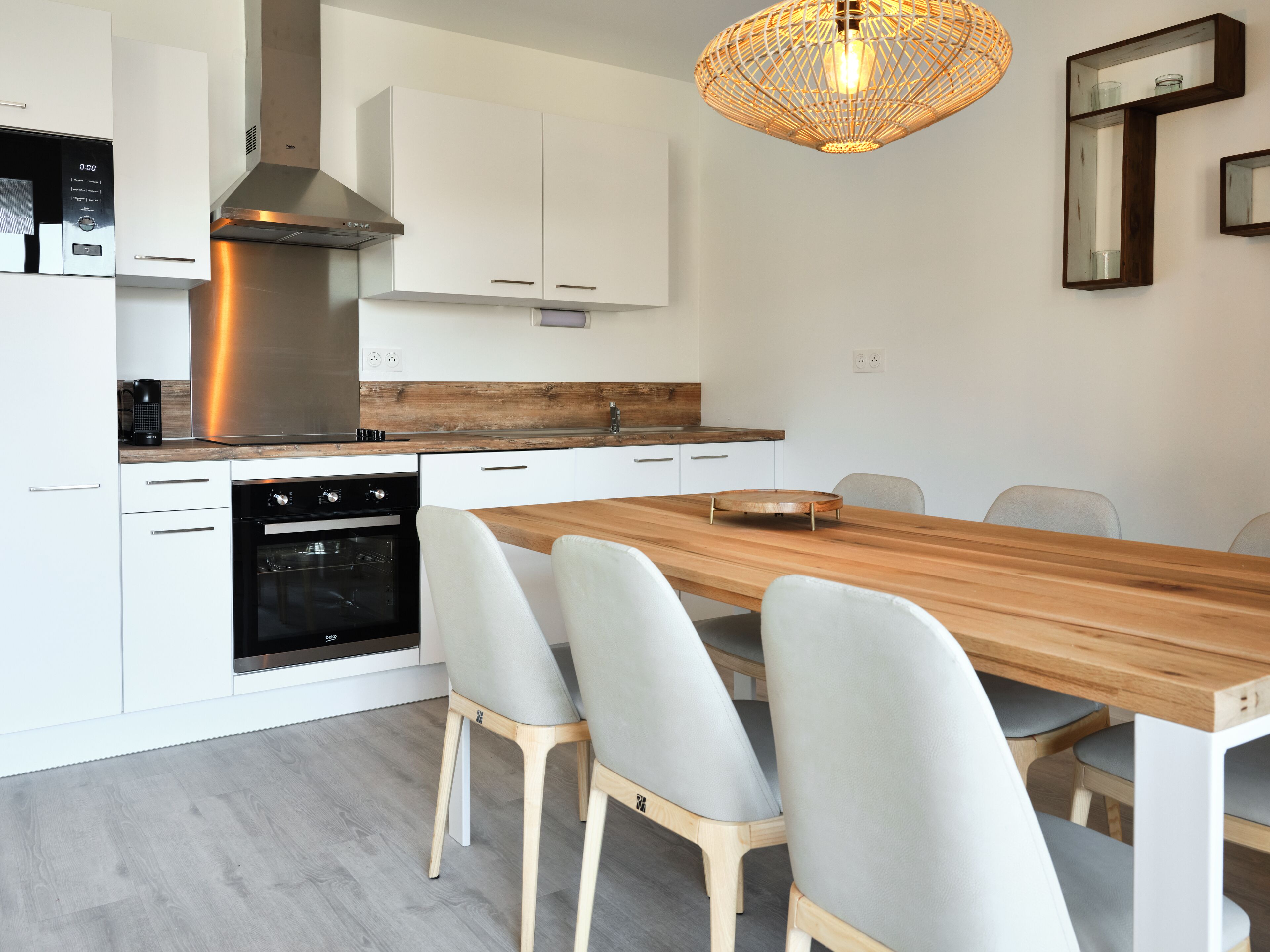 A modern kitchen with white cabinets, a wooden countertop, and a built-in oven. There are four chairs around a wooden dining table.