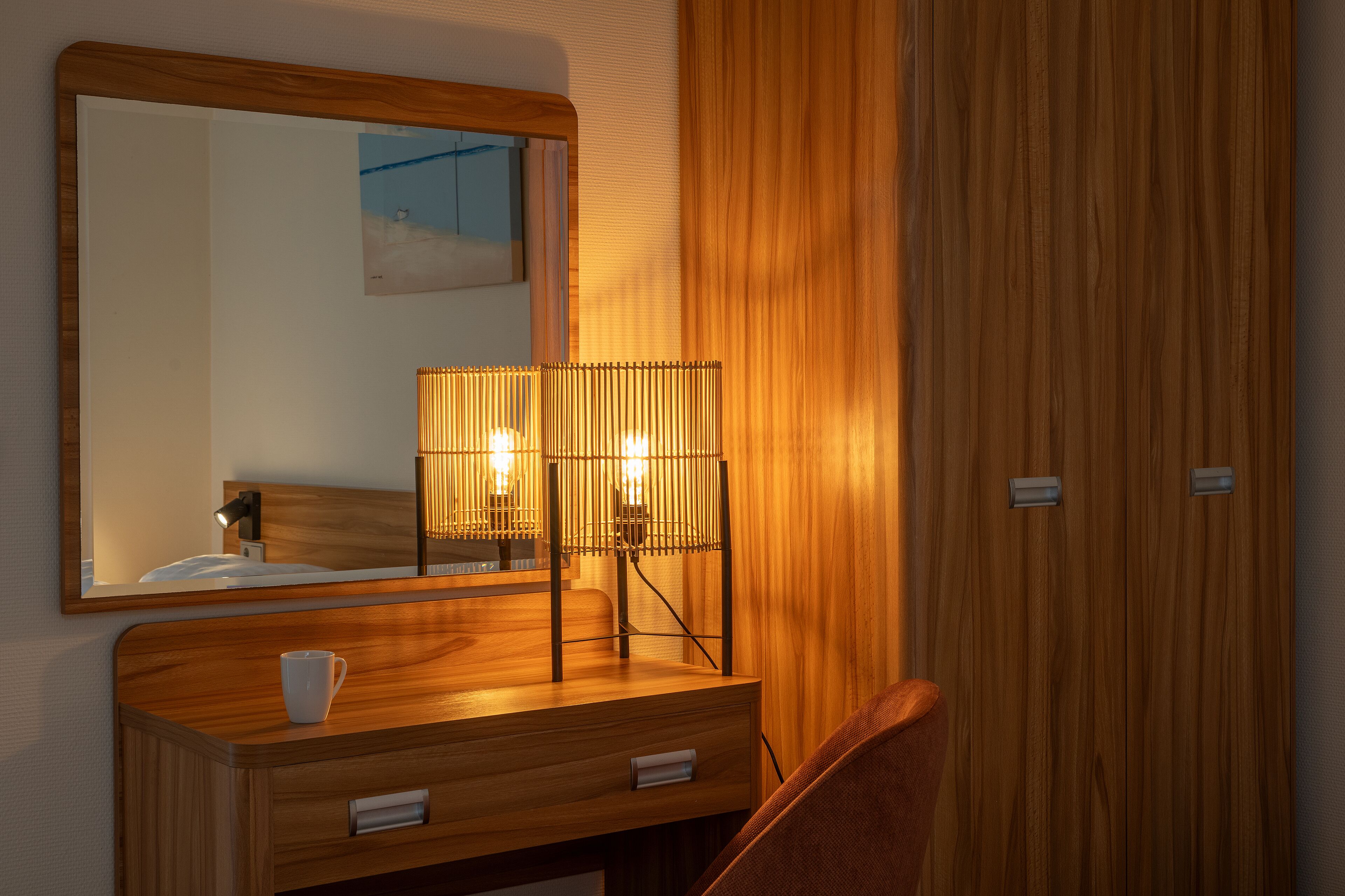 A wooden vanity with a mirror, a bedside lamp, and a cup on the counter.