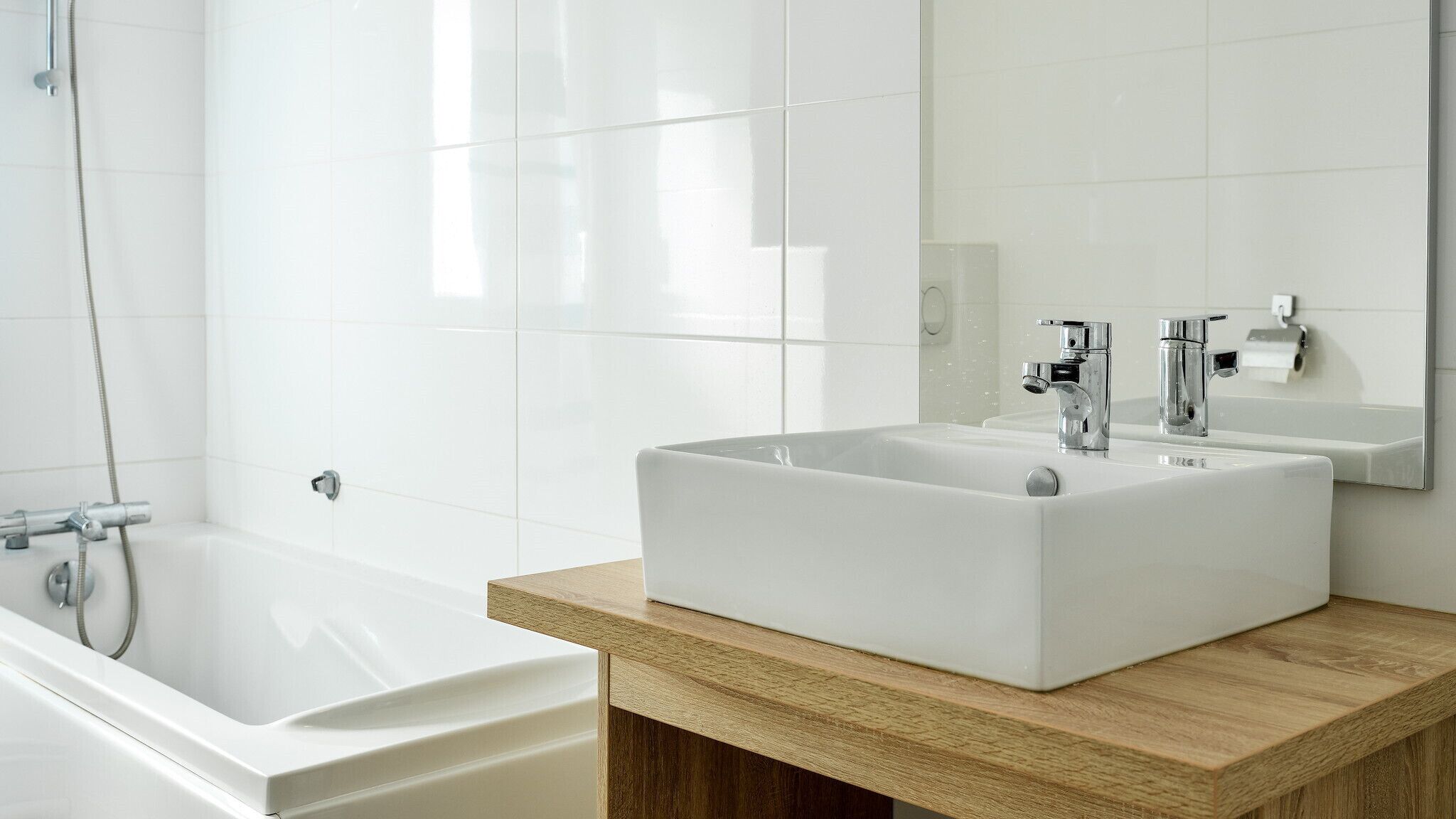Ein modernes Badezimmer mit zwei weißen Waschbecken, einer Holzablage, einem großen Spiegel und einer Badewanne.