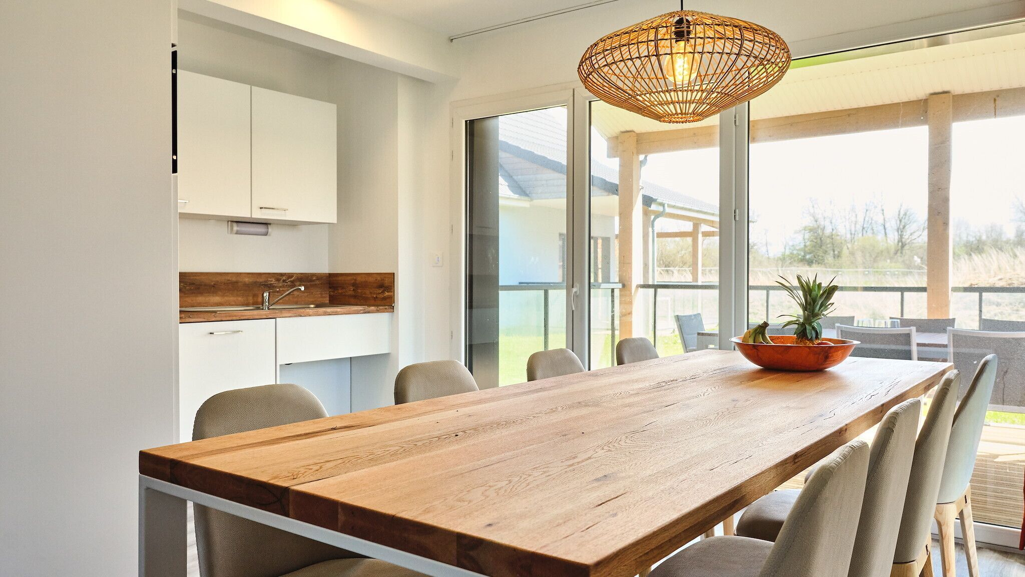 Una cocina moderna con armarios blancos, encimera de madera y una amplia mesa de comedor con sillas.