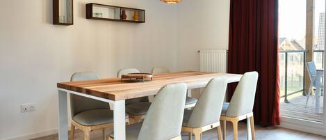 Un comedor con una mesa de madera y cuatro sillas, una lámpara colgante y vistas a un balcón a través de una ventana.