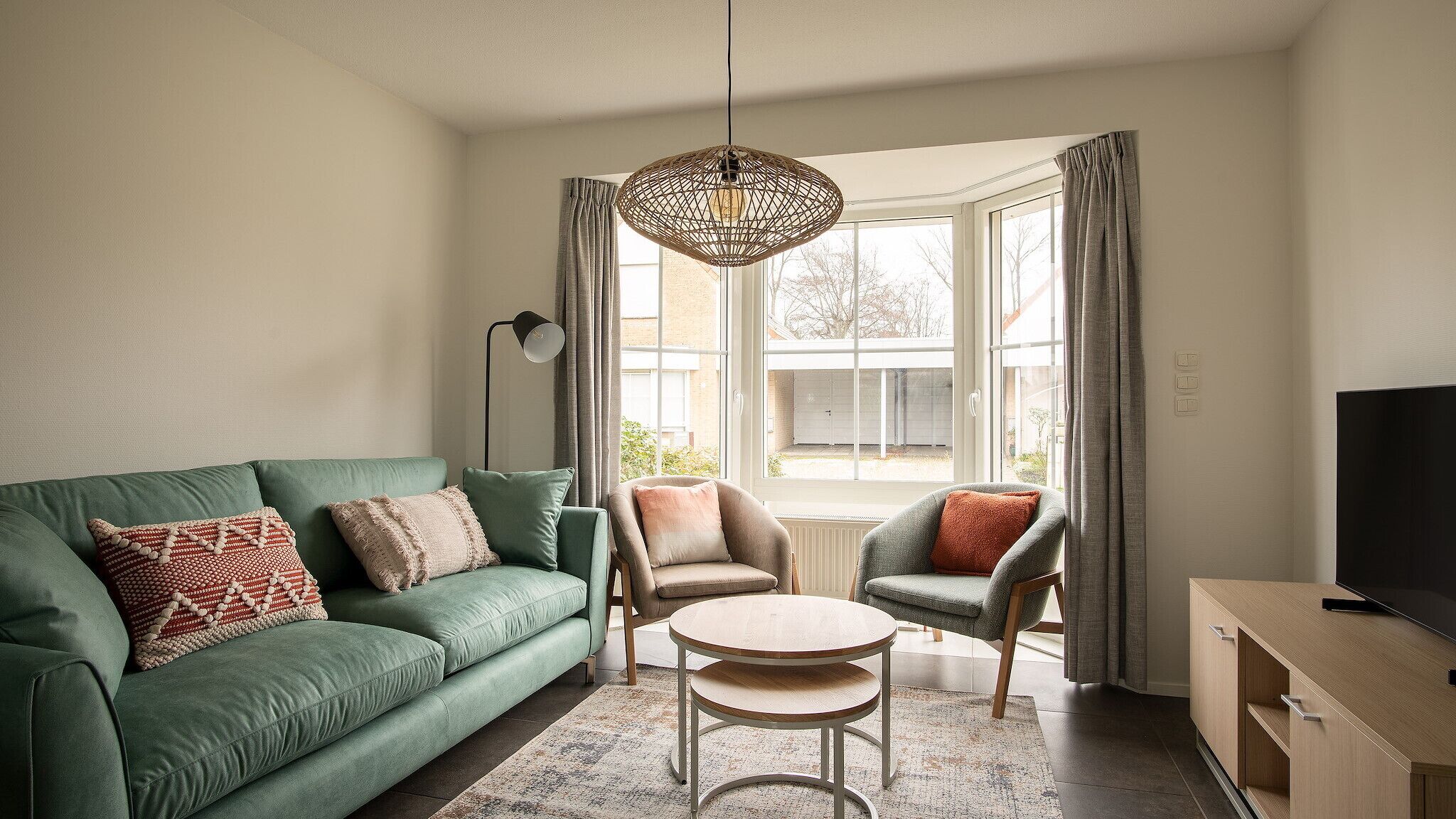 Un salon avec un canapé vert, deux fauteuils, une table basse et un téléviseur posé sur un meuble en bois.