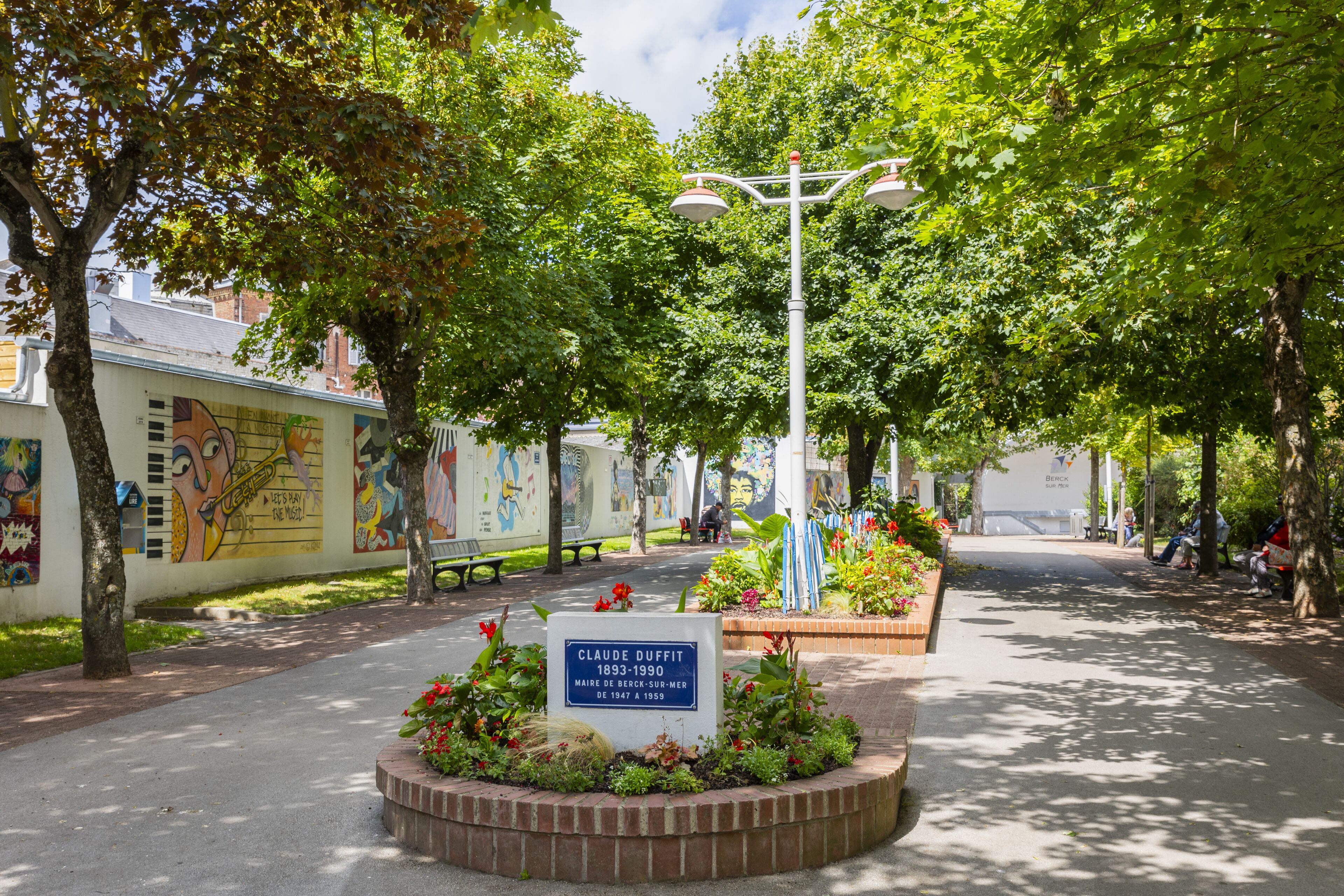 Un parc avec un parterre de fleurs circulaire, un lampadaire et une fresque murale.