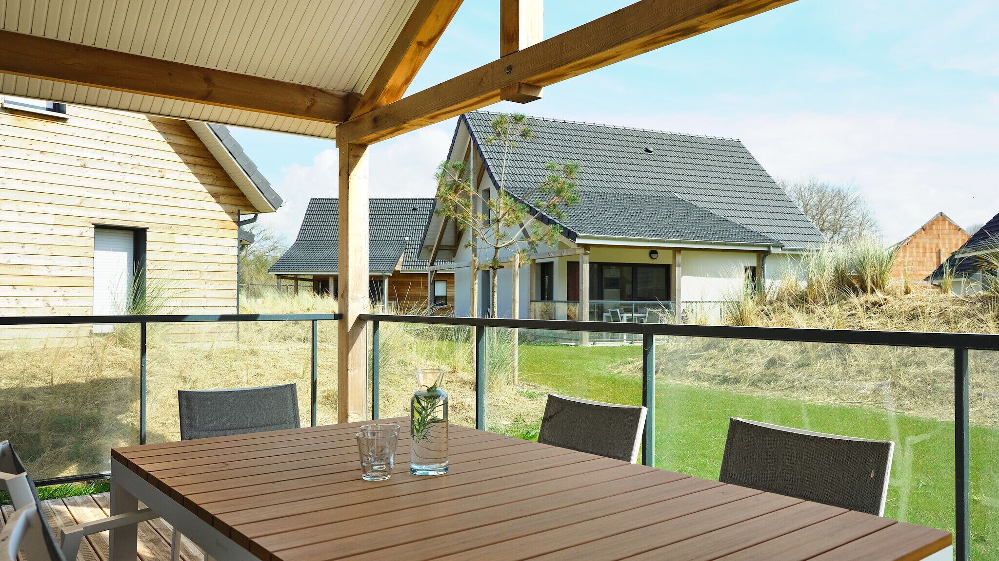 A wooden deck with a table and chairs, overlooking a grassy yard and houses.