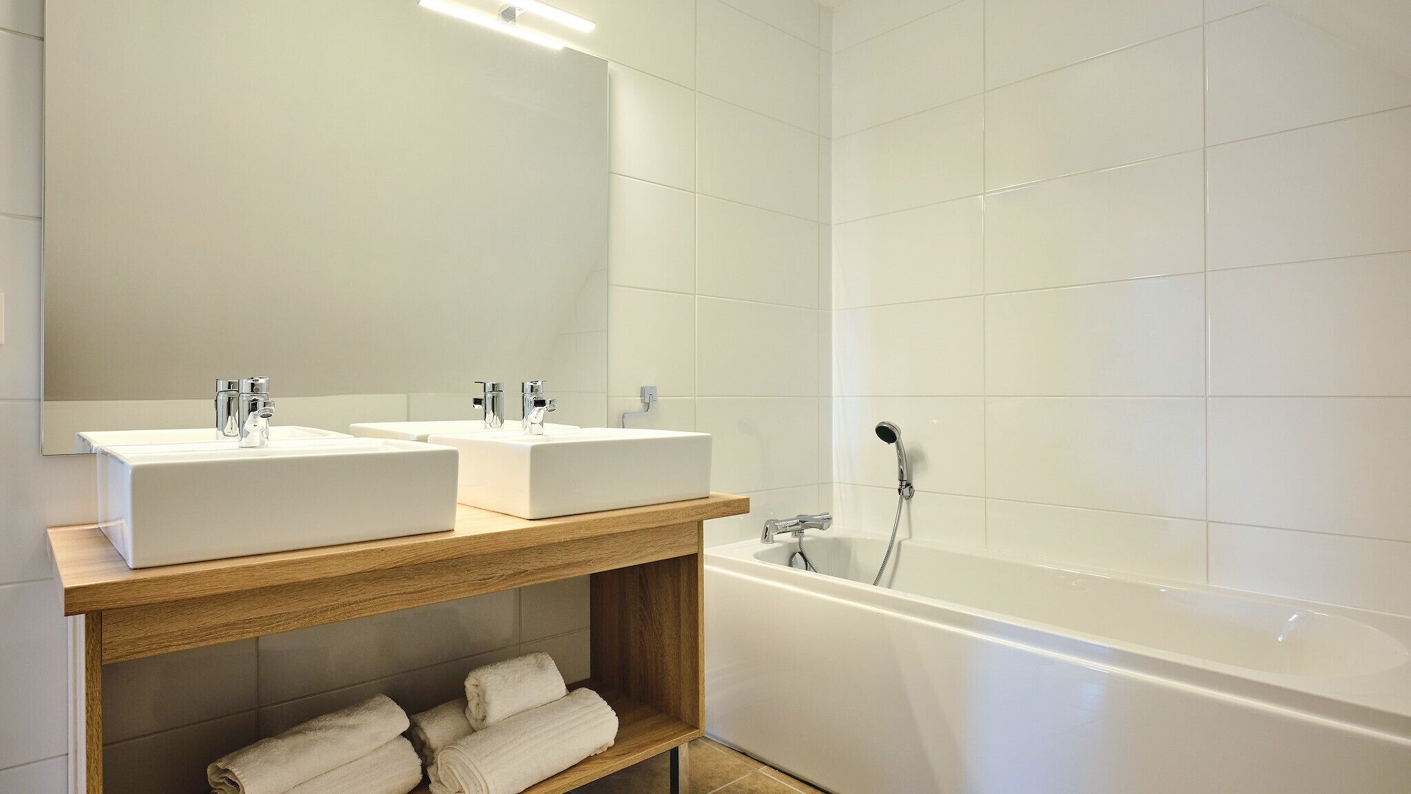 A modern bathroom with two sinks, a wooden vanity, and a freestanding bathtub.