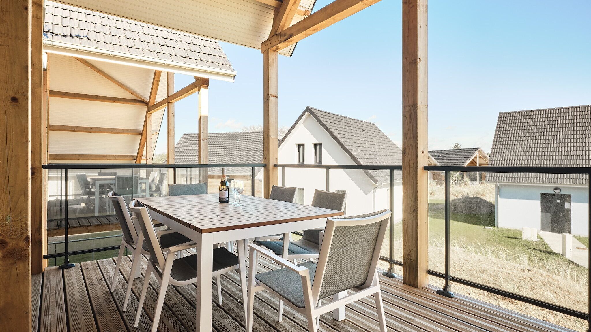Terraza de madera con mesa y sillas, con vistas a una zona residencial.