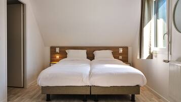Un lit double avec une tête de lit en bois, deux tables de chevet, un radiateur et une fenêtre avec des rideaux.