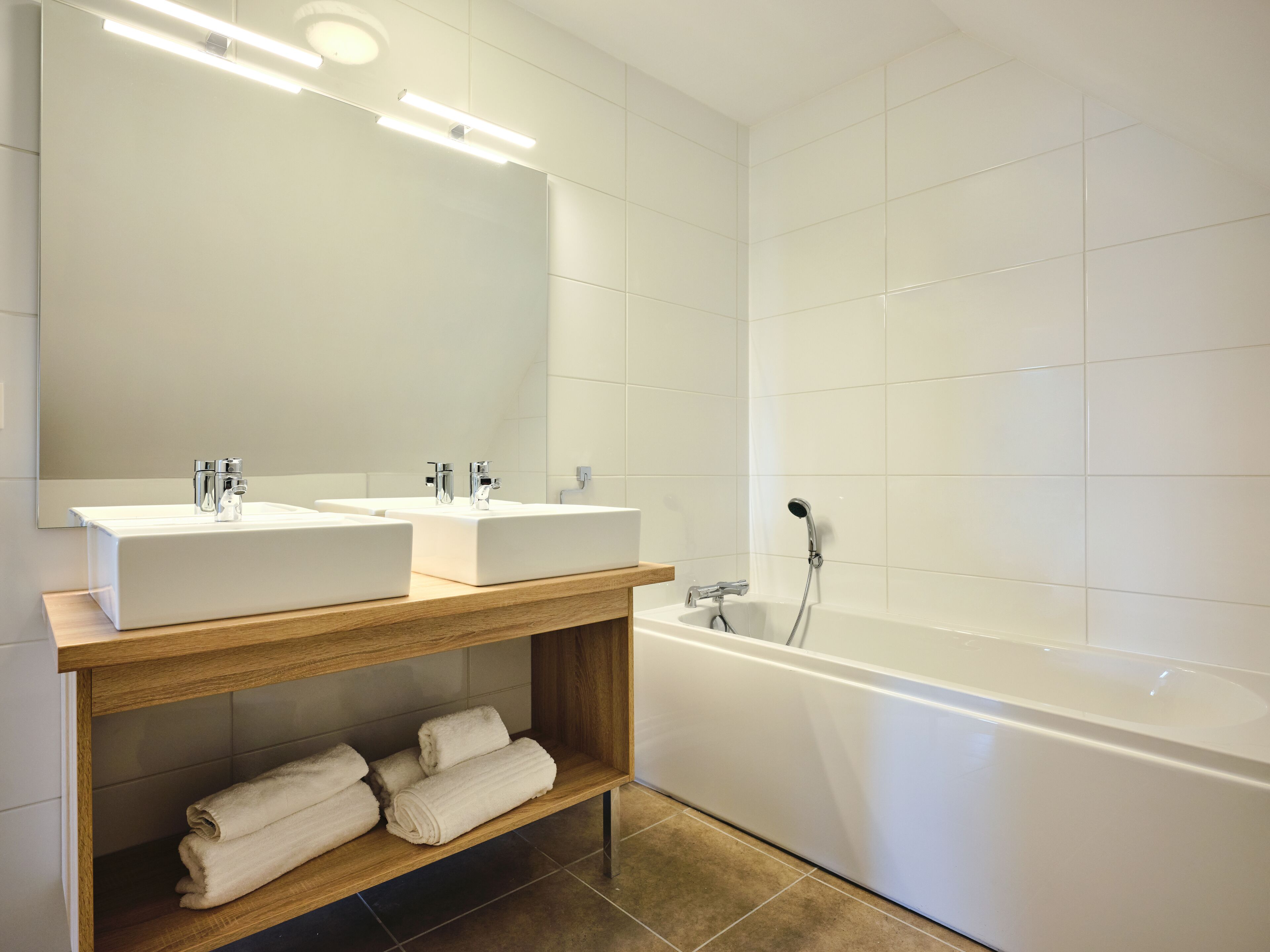 A modern bathroom with two sinks, a large mirror, and a bathtub.