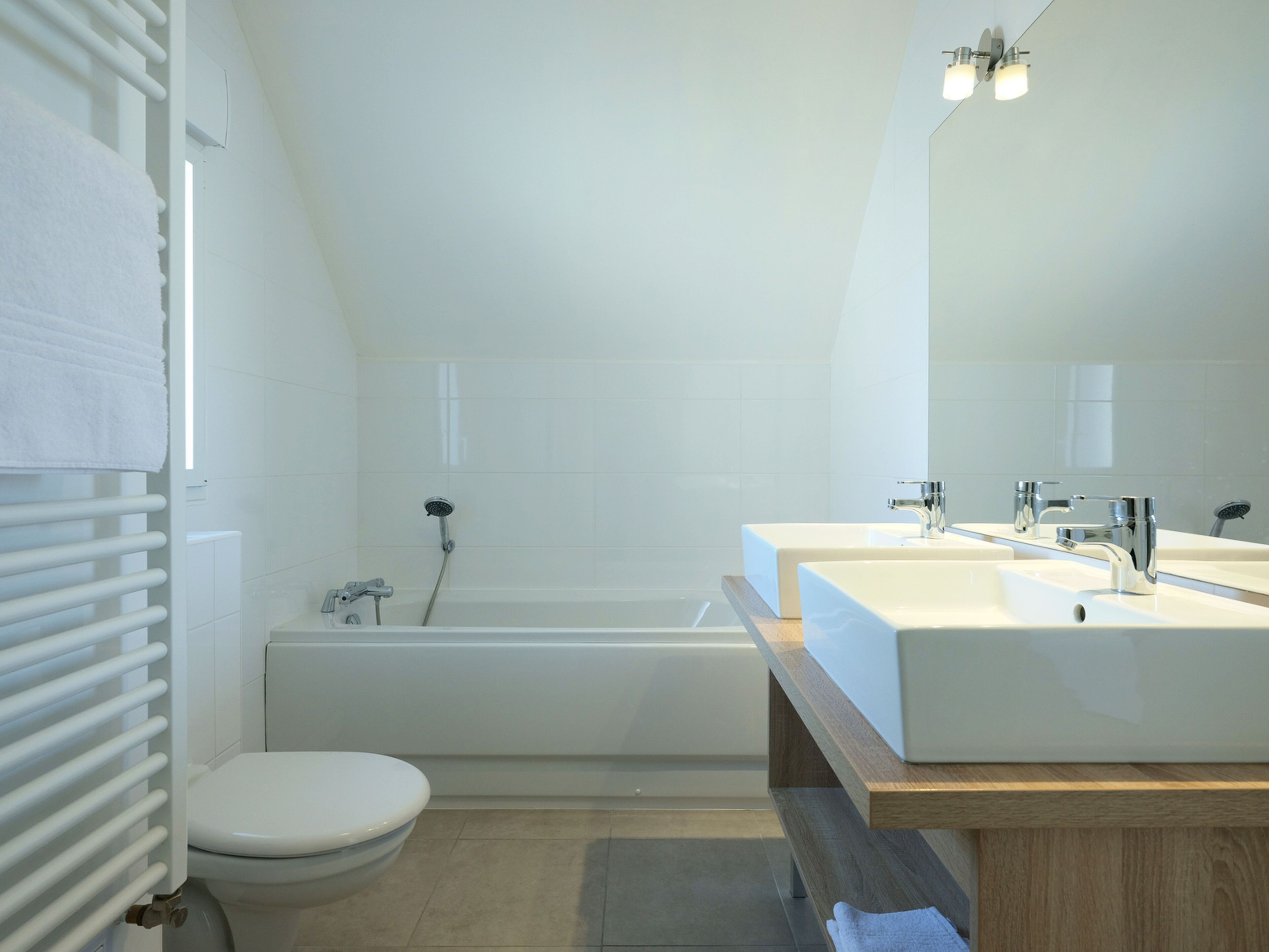 Een moderne badkamer met een badkuip, twee wasbakken en een toilet.