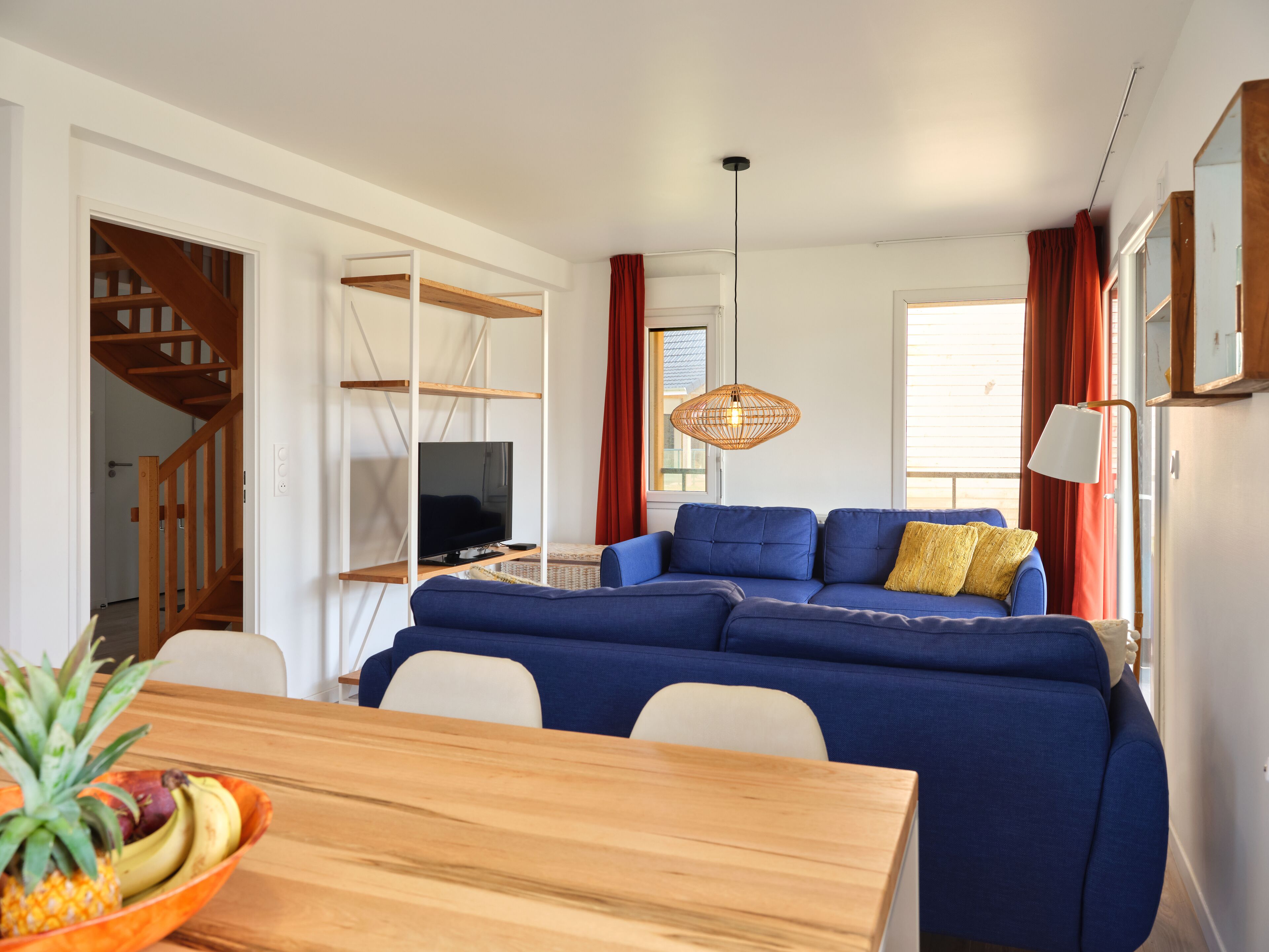 Un salon moderne avec un canapé bleu, une table à manger en bois et un téléviseur posé sur un meuble blanc.