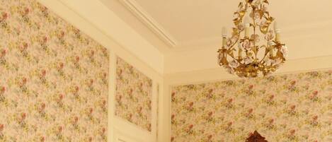 A bedroom with a large bed, floral wallpaper, a wooden wardrobe, and a chandelier.