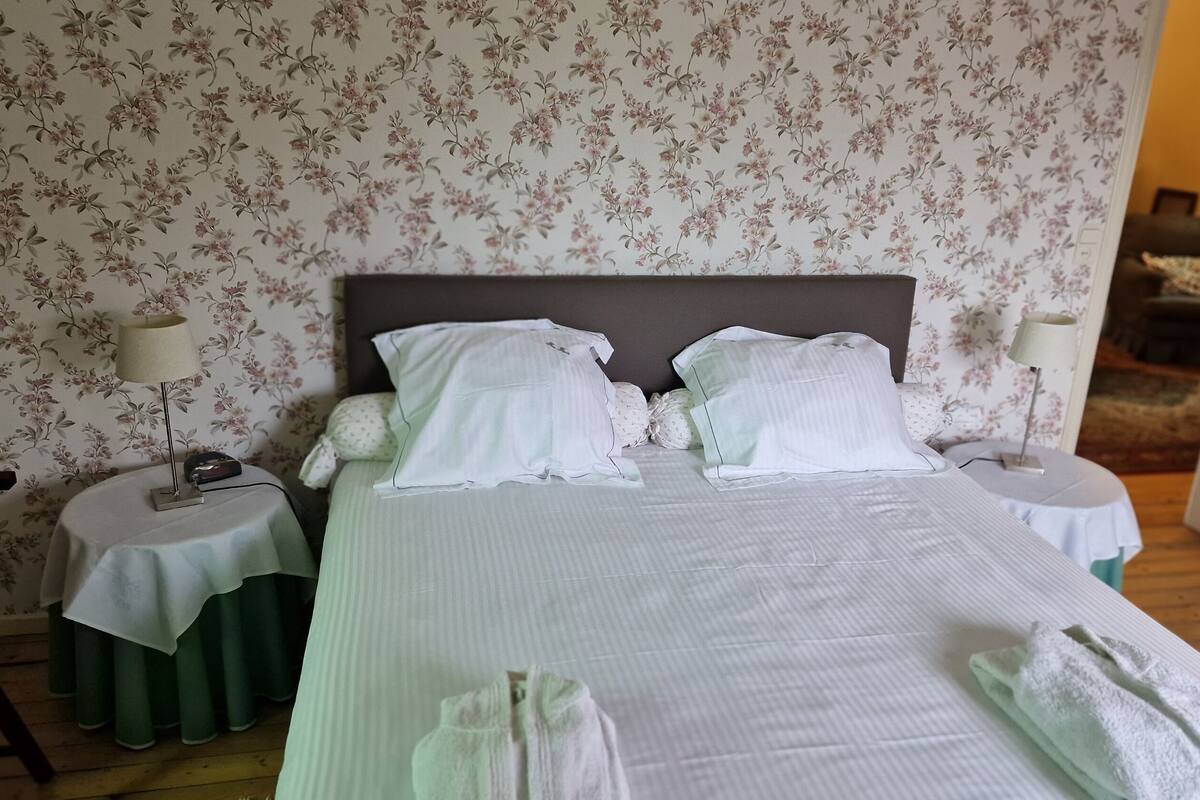 A neatly made bed with pillows and a blanket, two bedside tables with lamps, and floral wallpaper.
