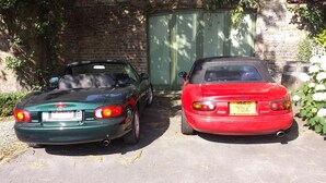 Two parked cars, a green convertible and a red sports car, in front of a brick wall with a green door and some greenery around. - Fine Fleur Bed & Breakfast (Bruges)