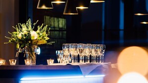 Un espace bar agrémenté de luminaires suspendus, d’un arrangement floral et d’une rangée de verres disposés sur une surface réfléchissante.
