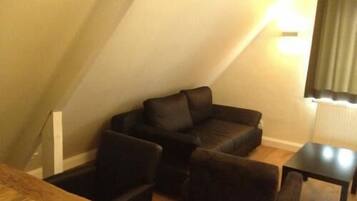 Una habitación pequeña y acogedora con un sofá marrón oscuro y dos sillones, una mesa de madera y una lámpara.