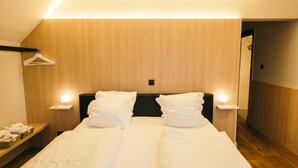 Une chambre d’hôtel avec un grand lit, deux tables de chevet, une tête de lit en bois et un porte-manteau mural.