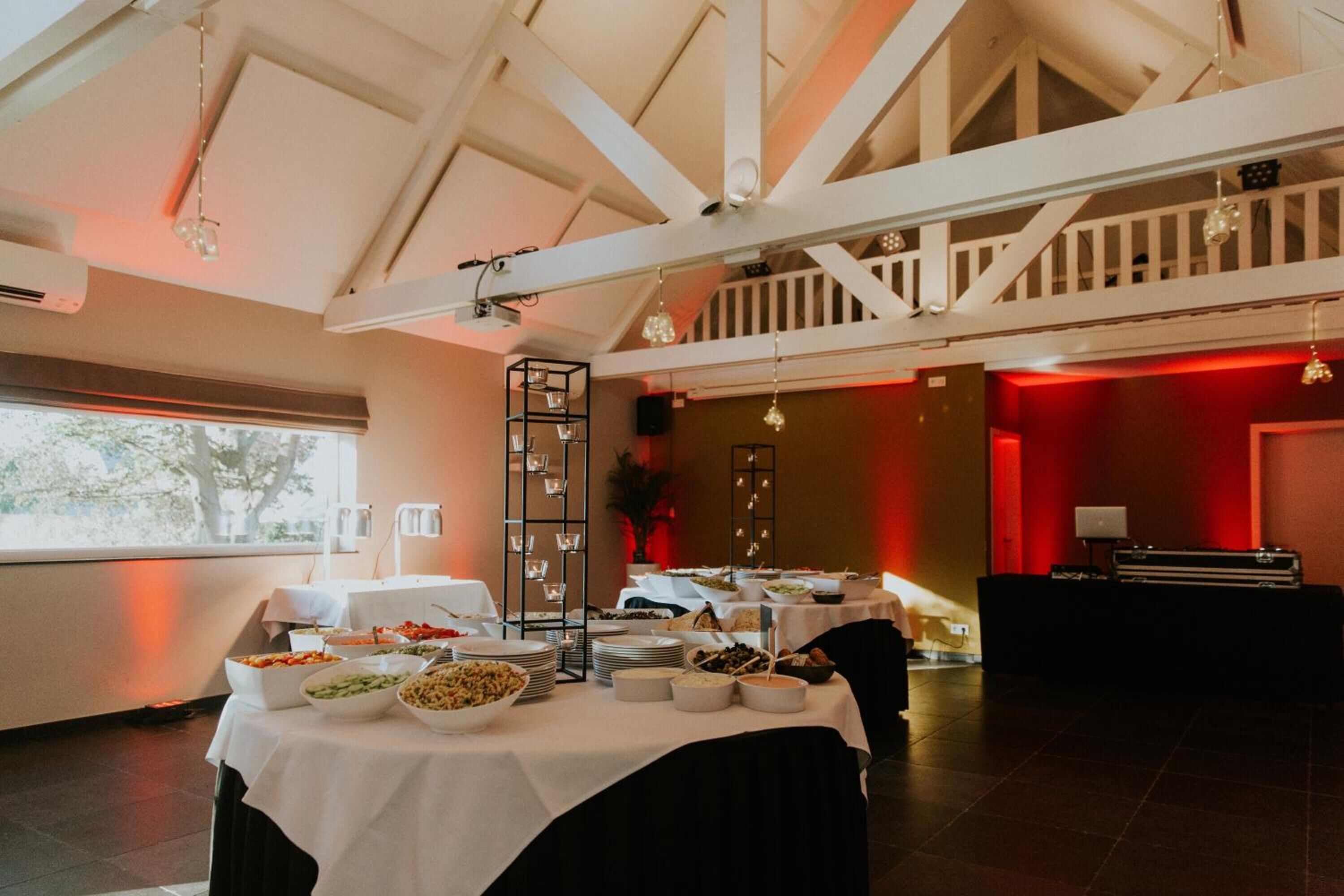 Un buffet est installé dans une pièce dotée d’un plafond haut et de poutres apparentes, et propose une variété de plats ainsi qu’un présentoir à étages pour les servir.