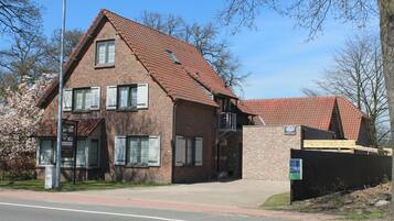 A two-story brick building with a red-tiled roof, a small porch, and a sign indicating a business or service.