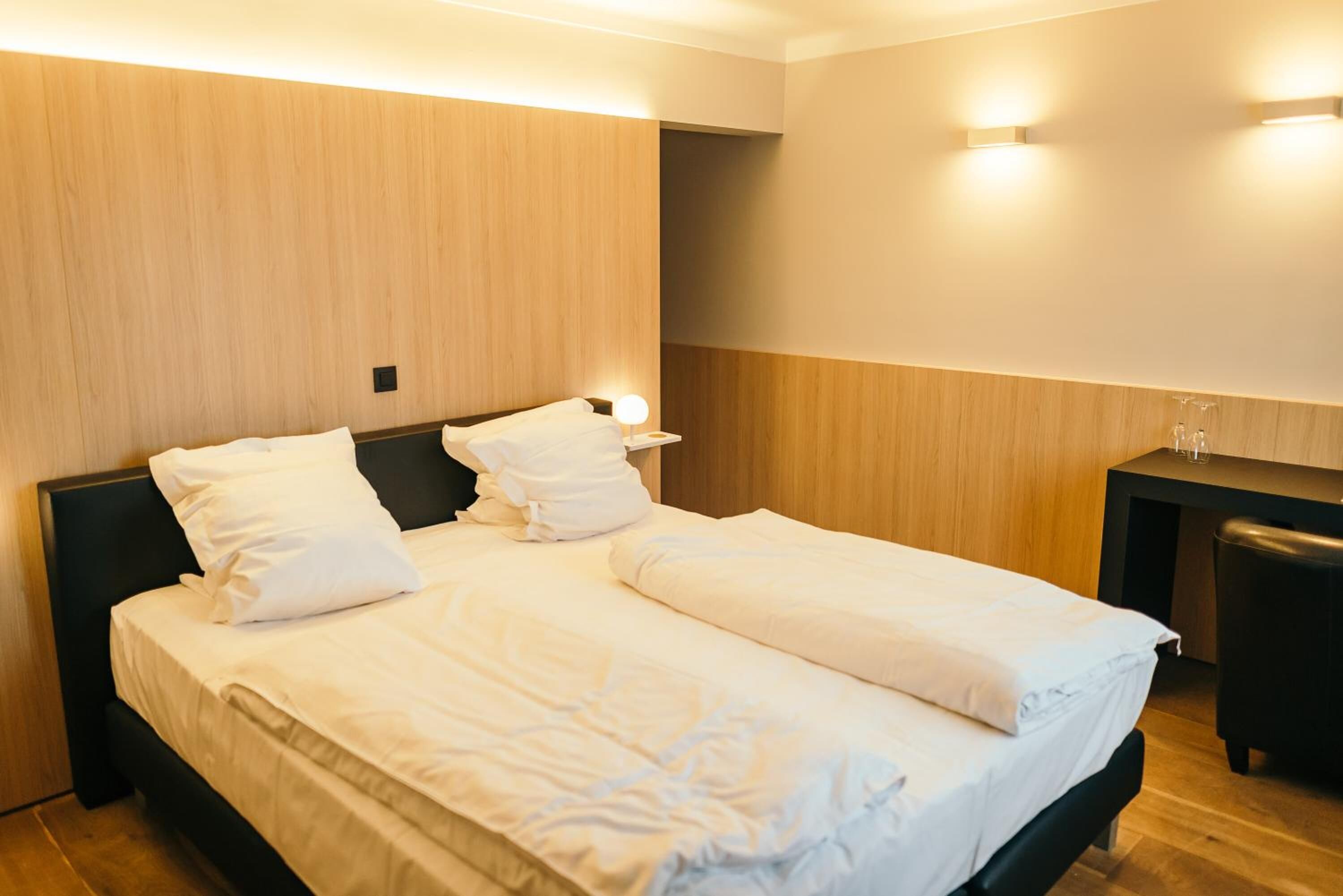 Un lit double avec du linge de lit blanc, une tête de lit en bois et une table de chevet avec une lampe.