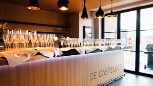 Un espace bar doté d’un comptoir en bois portant l’inscription « DE CASTELEER », de nombreux verres à vin et d’un éclairage suspendu.