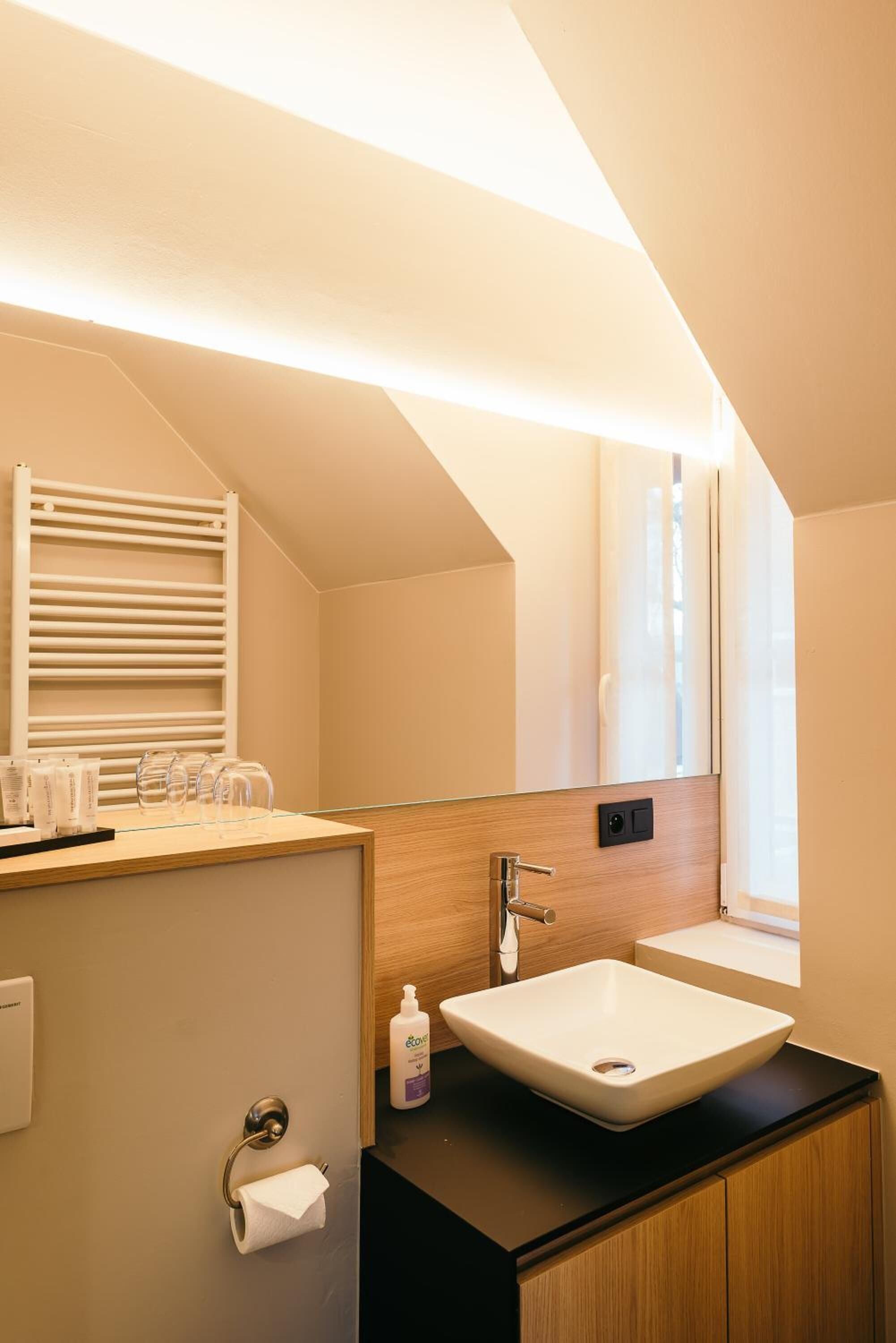 A modern bathroom with a large mirror, a wooden vanity, a sink, and a towel rack.