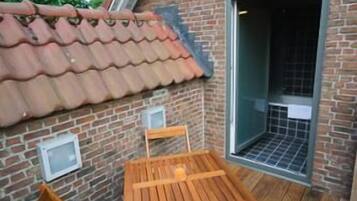 Una terraza de madera con una mesa y sillas, un muro de ladrillo y un tejado de tejas.