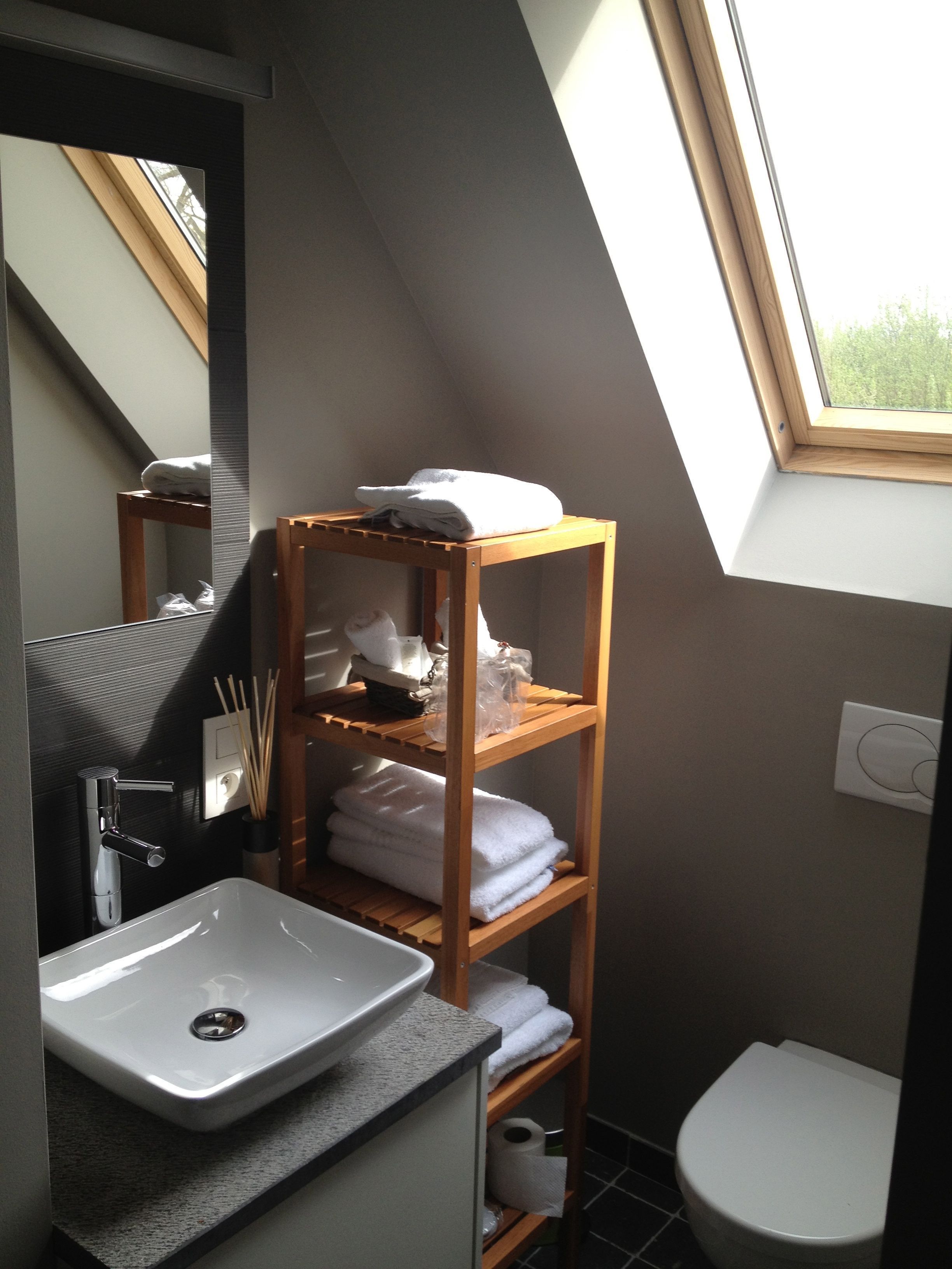 Une salle de bain moderne avec un puits de lumière, une étagère en bois avec des serviettes, un lavabo et des toilettes.