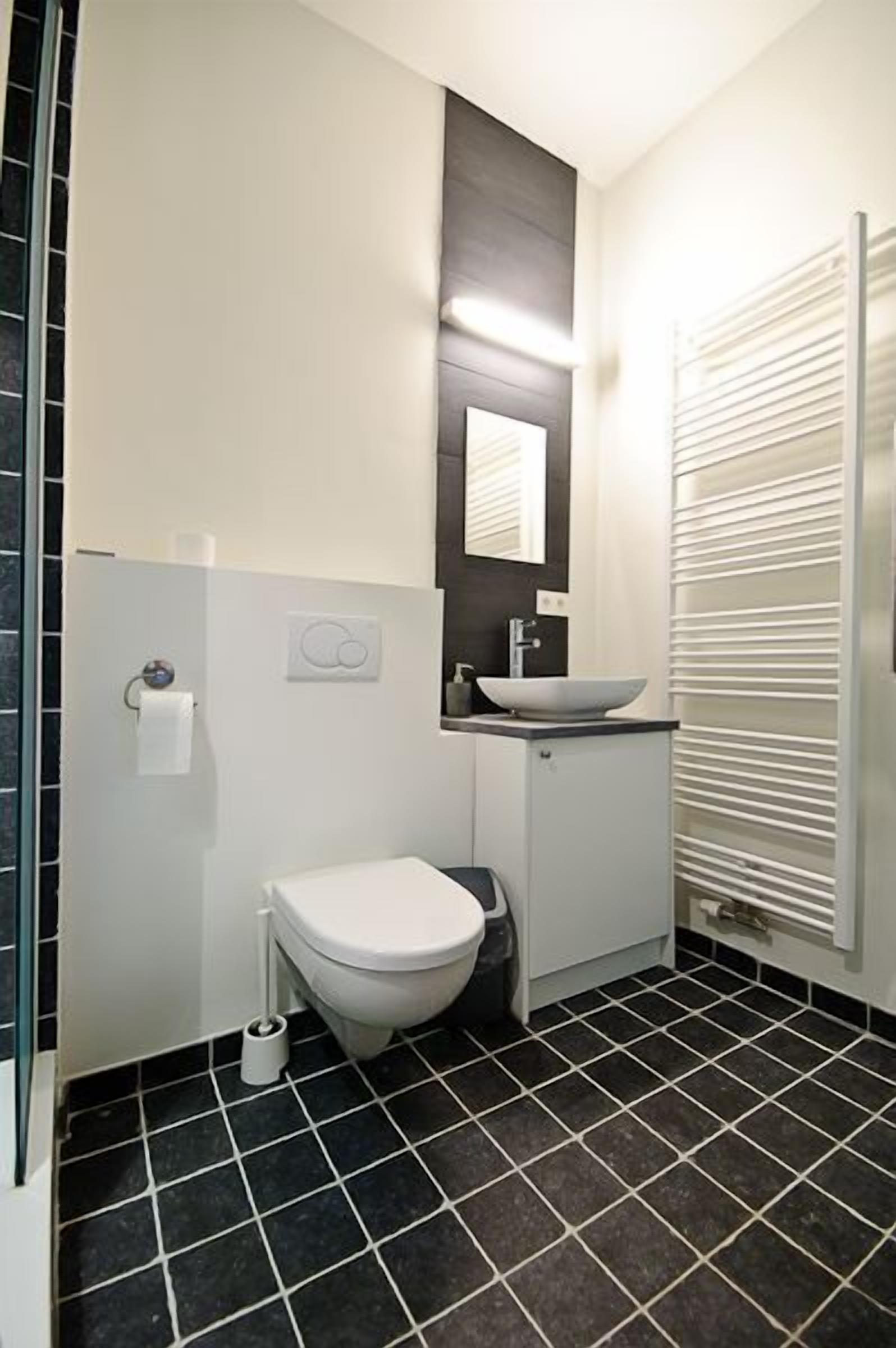 A modern bathroom with a white toilet, a vessel sink, and a mirror above it.