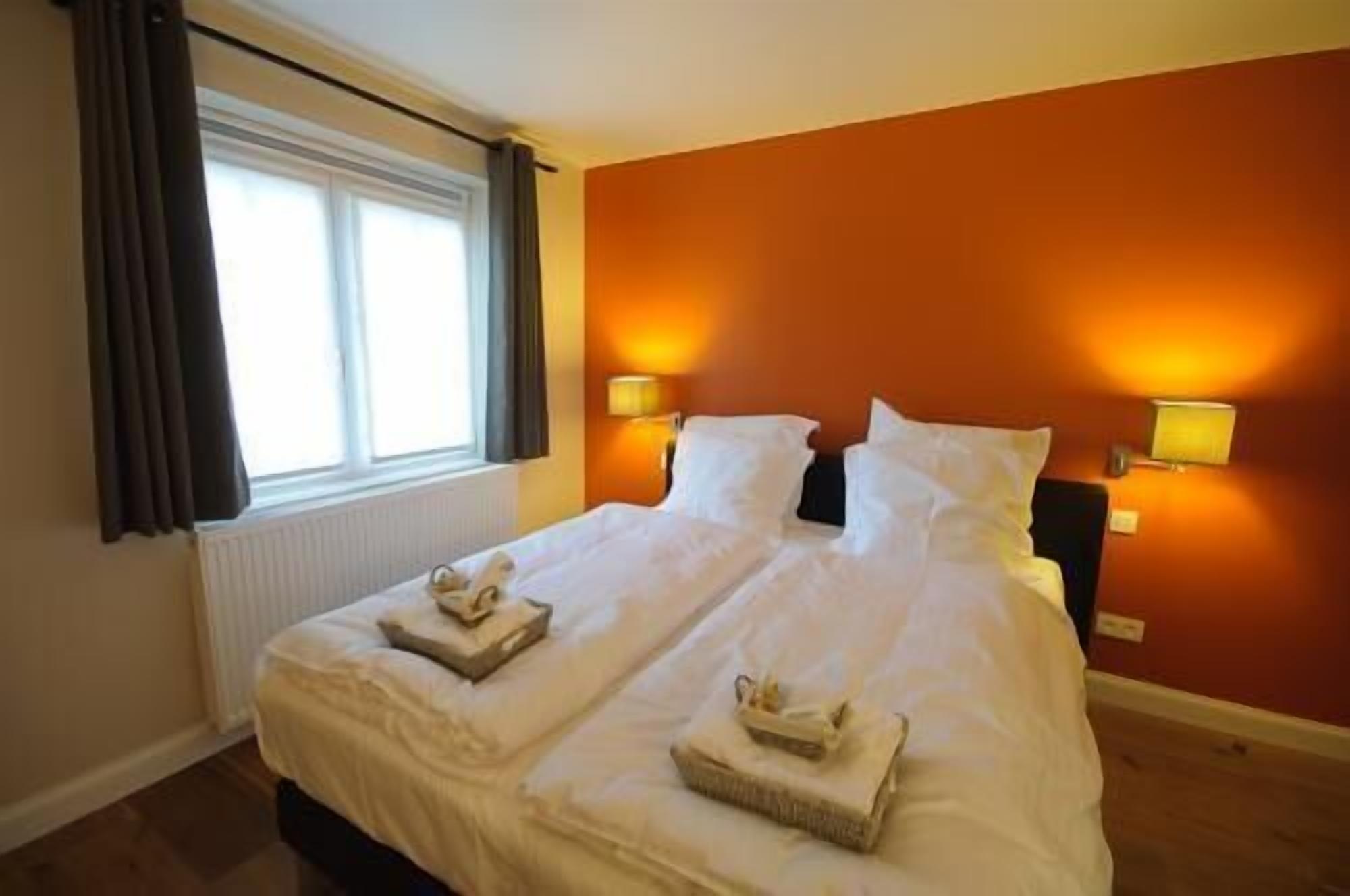 A hotel room with a large bed, two bedside lamps, and a window with curtains.