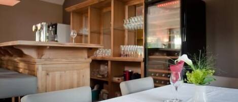 A restaurant with a white table set for two, a wooden bar area, and a refrigerator stocked with beverages.